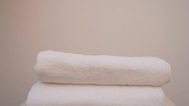 Woman puts four folded white cotton towels in stack. 4k stock video footage of pile of 4 towels laying on table isolated on white wall background