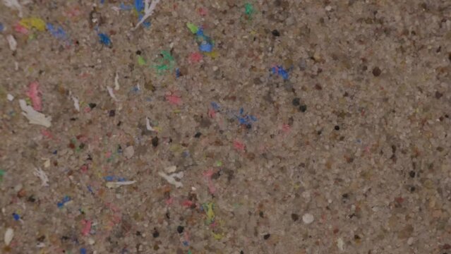 Micro plastic on the sand of the beach, close-up. Fragments of plastic on the beach in the wind. Plastic pollution in the environment. Top view.