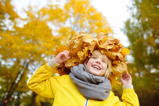 Cute little boy with a wreath of maple leaves on his head on sunny autumn day. Child having fun during stroll in the forest. Active outdoors leisure for children