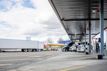 Big rigs semi trucks with semi trailers standing on the truck stop fuel station refueling tanks for...