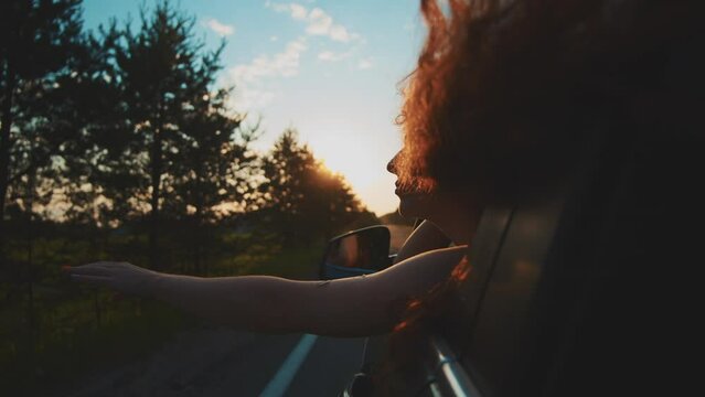 Happy woman in car window. Hair in wind. Girl travels by car. Hand in sun. Windy breeze from car window. Happy female smiling from car window. Windy breeze in your hair. Hand in the rays of the sun