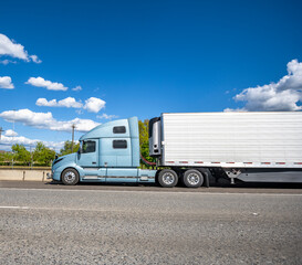Blue big rig semi truck with refrigerator semi trailer transporting cargo driving on the wide multiline highway