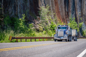 Blue big rig tipper semi truck with two tip semi trailers running on the winding mountain road in Columbia Gorge