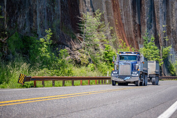 Blue big rig tipper semi truck with two tip semi trailers running on the winding mountain road in...