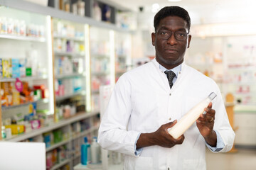 Portrait of african american male pharmacist working in pharmacy demonstrating goods while standing in sales floor