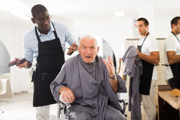 Silver haired senior man unpleasantly surprised by haircut from African-American hairdresser in hair salon