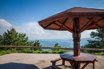 Picnic wooden table with a wood umbrella and benches in front of a panorama of the divcibare mountains and the tometino polje plain in Divcibare, a major mountain resort of Serbia...