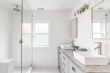 An elegant, renovated bathroom with white sinks, grey vanity, granite countertop, and bronze...