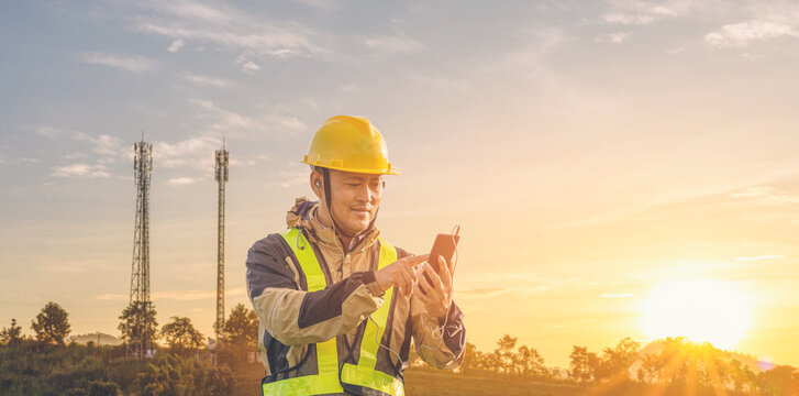 Engineer manager worker speaking on mobile phone with telecommunication antenna and sunset background.