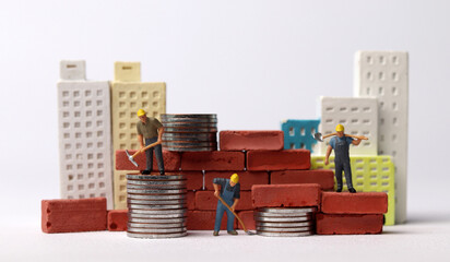 Miniature workers building bricks. Business concept with coins and miniature people.
