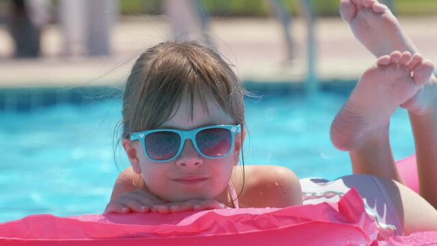 Young child girl relaxing on summer sun swimming on inflatable air mattress in swimming pool during tropical vacations. Summertime activities concept
