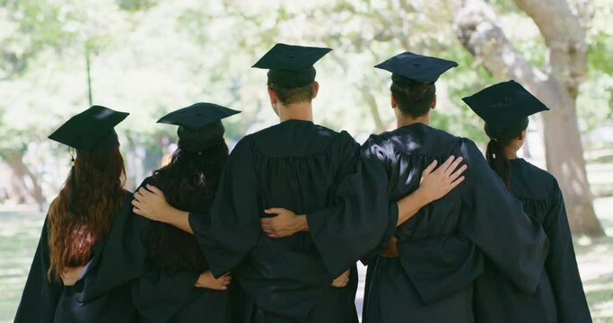 Rear of students standing together at graduation. Group of successful graduates embracing in unity with cap and robe and feeling accomplished having achieved their diploma certificates at university