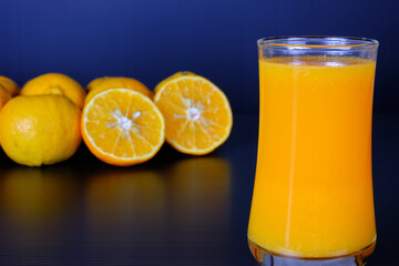 Close-up and vivid studio shot, a glass of orange juice, and a group of natural fresh oranges on black background, organic beverage, delicious healthy refreshment, and tasty vitamin nutrient drink.
