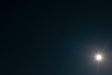 Fototapeta na wymiar Night sky background with moon shining like a big star on black sky with a stars. Astro photo on summer night