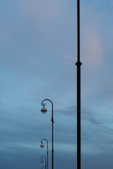 Beautiful black lanterns on tall poles along the pedestrian walkway on a cloudy sky