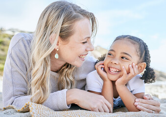 Mature foster mother and her adopted daughter smiling and lying on the beach together. Woman and...