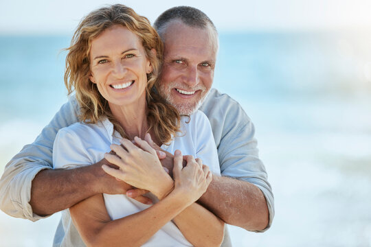 Portrait Of Happy And Loving Retired Mature Caucasian Couple Enjoying A Romantic Date At The Beach On A Sunny Day. Cheerful Affectionate Husband Hugging His Wife While Enjoying Seaside Vacation