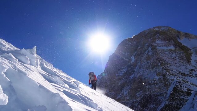Climber reaches the summit of mountain peak. Climber on the snow range moving forward while selfbelaying with ice axe. Success, freedom and happiness, achievement in mountains. Climbing sport concept.