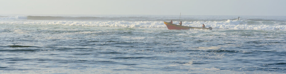 from the beach: red fishing boat in rhe waves on the sea