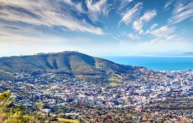 Copy space with cloudy blue sky over the view of a coastal city seen from Signal Hill in Cape Town South Africa. Scenic panoramic landscape of buildings in an urban town along the mountain and sea