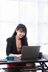 Portrait of a smiling Asian Business woman using modern technology, working over the laptop.