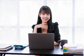 Portrait of a smiling Asian Business woman using modern technology, working over the laptop.