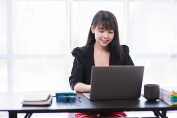 Portrait of a smiling Asian Business woman using modern technology, working over the laptop.