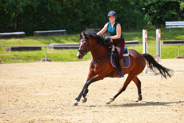 Young rider gallops her horse across the riding arena and smiles at the camera..
