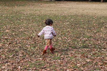 落ち葉のある広場を駆け回る小さな女の子