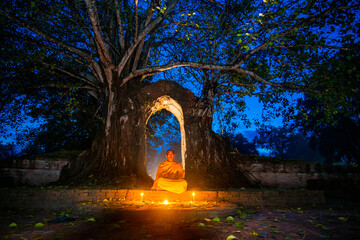 A Thai monk made meditating at an abandoned temple, the old entrance has a banyan tree. Landmark of the ancient city of Ayutthaya, Thailand.