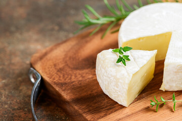 Sliced Camembert Cheese with thyme on wood plate. Camembert is a moist, soft, creamy,