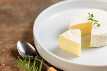 Sliced Camembert Cheese in white dish with spoon on table.