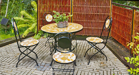 Garden chairs and table in serene, peaceful private home backyard. Wrought iron metal patio...