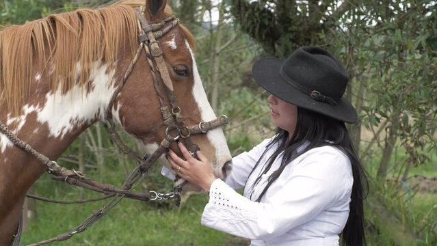 Slow motion video of latina cowgirl petting her horse.