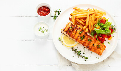 Salmon steak with vegetables and fries on light background.