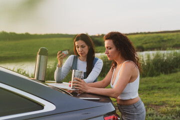 Fototapeta premium two girls are traveling on the roads by car, stopped at the side of the road and look at the map, drinking coffee from a thermos. Vacation concept