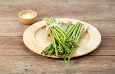 Asparagus is green and straight vegetable. Fresh, green asparagus is crispy for cook on wood table with salt