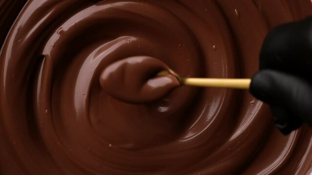 Hand stirring melted dark chocolate with golden spoon, close up. Liquid hot chocolate. Confectioner prepares chocolate dessert, glaze