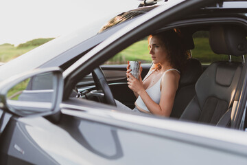 Naklejka premium beautiful young woman travel on the roads by car, stopped at the side of the road and look at the map, drink coffee from a thermos. Vacation concept