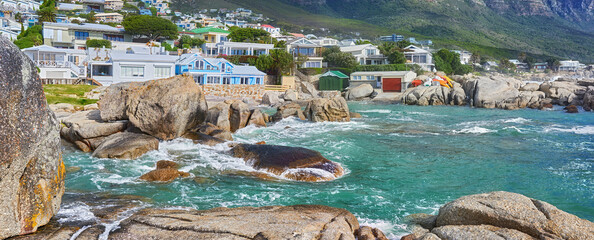Schilderachtig uitzicht op zee, rotsen en woongebouwen in Camps Bay Beach, Kaapstad, Zuid-Afrika. Getijde oceaangolven wassen over kustlijn rotsen en keien. Overzeese reizen en toeristische bestemming