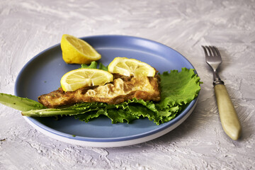 fried fish with lemon and herbs on a plate and a fork on the table