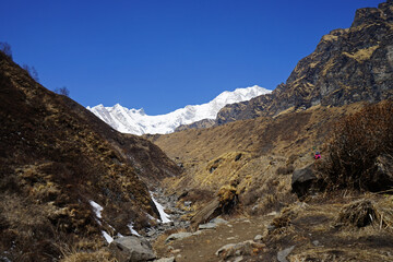 Rocky trail pathway with natural landscape view of snowcapped mountain range with cloudy blue sky- Himalayas ridge, Nepal