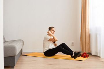 Fototapeta premium Side view of sick woman sitting on yoga mat feeling elbow pain while doing exercise for good body shape at home, touching painful place, frowning face, being injured during workout.