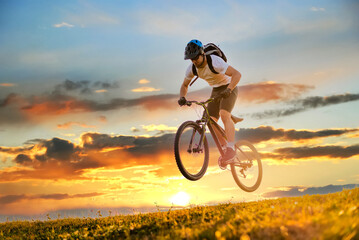 A mountain bike cyclist jumping while trail riding downhill on the sky sunset background. Action...