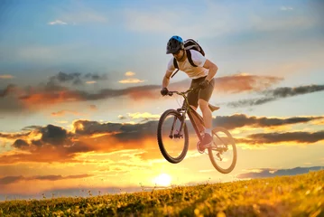 Fotobehang A mountain bike cyclist jumping while trail riding downhill on the sky sunset background. Action extreme sport outdoor. Active healthy lifestyle. Young man rides bicycle in nature. Adventure travel. © Malik Nalik