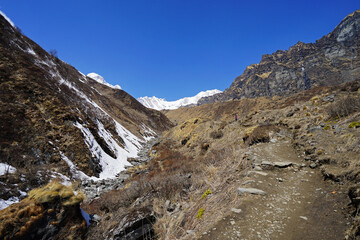 Rocky trail pathway with natural landscape view of snowcapped mountain range with cloudy blue sky- Himalayas ridge, Nepal