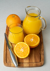Glass and jug with orange juice on a wooden stand, sliced orange, background line
