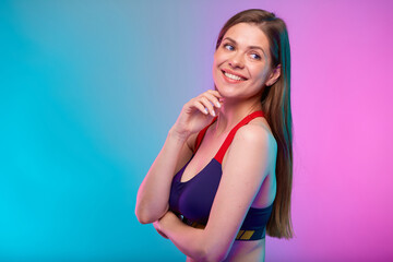Thinking happy sporty woman in fitness bra sportswear looking up with mouth open. Female fitness portrait isolated on neon multicolor background. Girl face with hand touching chin.