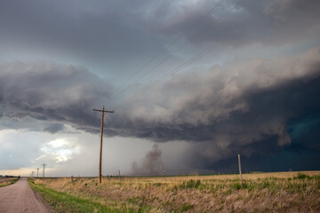 A severe thunderstorm produces winds that lift dust and dirt upwards into the storm cloud, with a gravel road and power lines in the foreground.