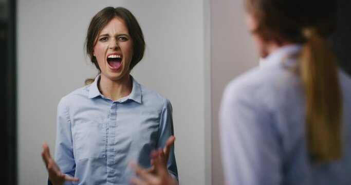 Scared schizophrenia patient shouting while looking in an asylum mirror. Woman suffering from bipolar disorder, feeling stressed, anxious, crazy. Mentally ill with dissociative personality disorder